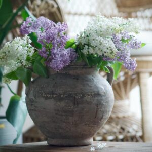 Terrakottakrukan KATE från Wikholm form, fylld med vackra vita och lila syrenblommor, står på ett bord i en ljus och inbjudande inomhusmiljö.