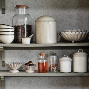 Beige skål INGRID från Strömshaga pryder en rustik hylla, omgiven av andra köksdetaljer. Perfekt för att skapa en varm och hemtrevlig känsla i ditt kök.