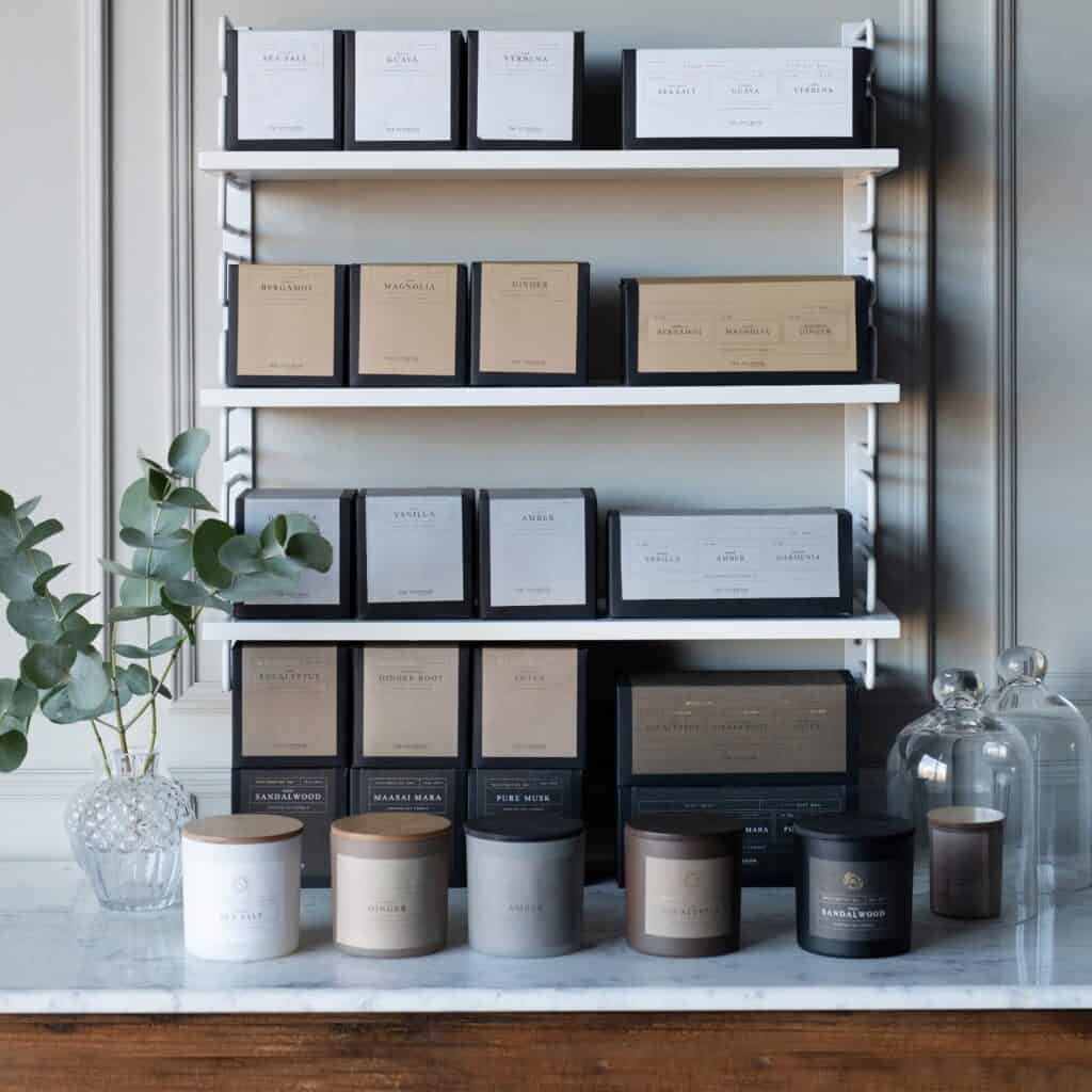 Hylla med doftljus från Wikholm Form, inklusive doftljuset SANDALWOOD, i en elegant miljö med växter och stilren inredning.