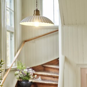 Taklampan INGRID i antik vit från varumärket Strömshaga hänger i en ljus och charmig trappuppgång med trädetaljer och blommor i en vas på ett trappsteg.