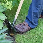 Person använder en halvmåneformad kantskärare från Burgon & Ball för att skapa en rak kant mellan gräsmatta och rabatt.
