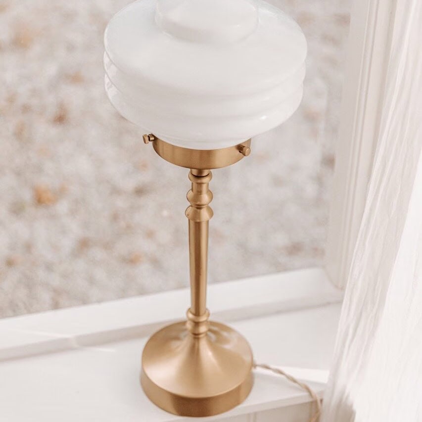 Närbild på VALTER bordslampa från Strömshaga, elegant design med mässingsfot och rund vit opalglasskärm.