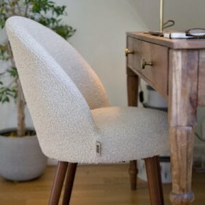 Stol BARBARA i beige bouclé placerad vid skrivbord i trä – varm och naturlig miljö.
