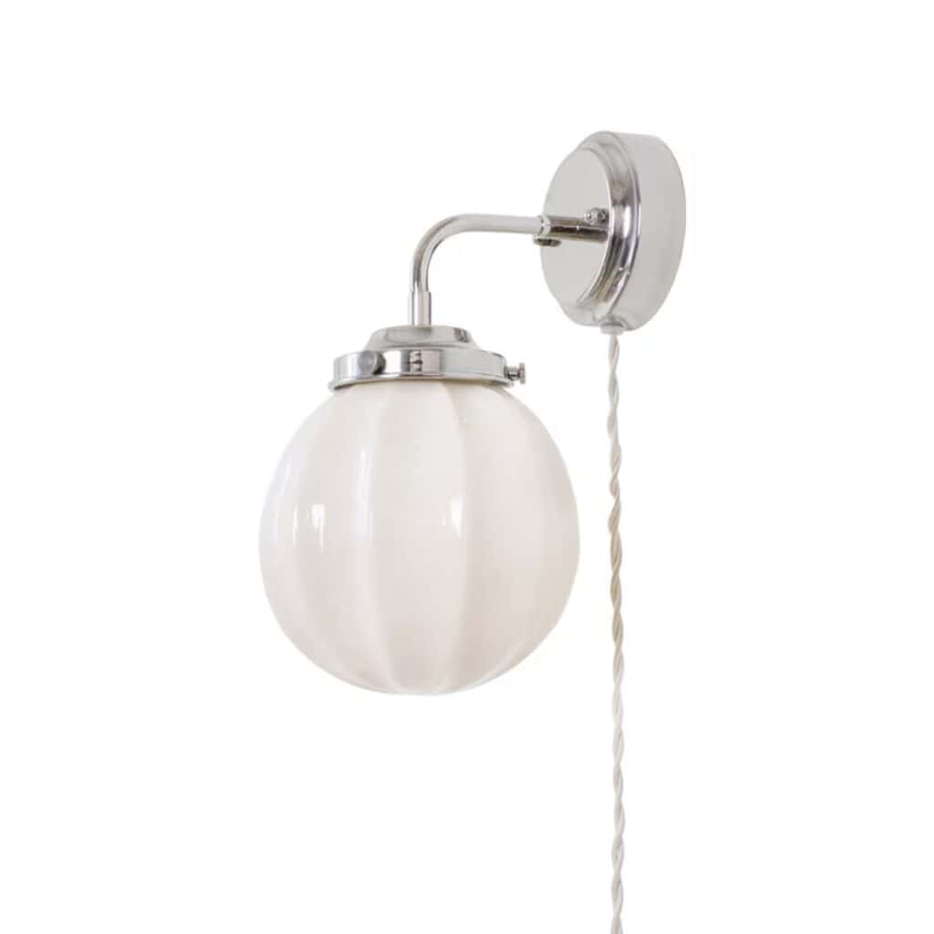 Vägglampa Marit från Strömshaga med förnicklad metall och rund opalglas kupa, beige textilsladd, sedd från sidan.