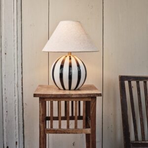 Lampskärm Hedvig i beige linnetyg från Strömshaga placerad på en svart-vit randig lampfot, skapar en mysig och tidlös atmosfär.