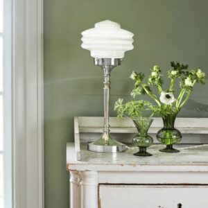 Bordslampa Valter från Strömshaga i förnicklad metall med vit opalglas-kupa, placerad på en vit vintagebyrå mot en grön vägg och dekorerad med gröna glasvaser och blommor.