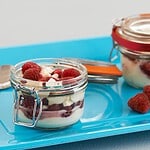 Kilner glasburk fylld med en dessert av färska hallon, grädde och maräng, serverad på ett blått fat.