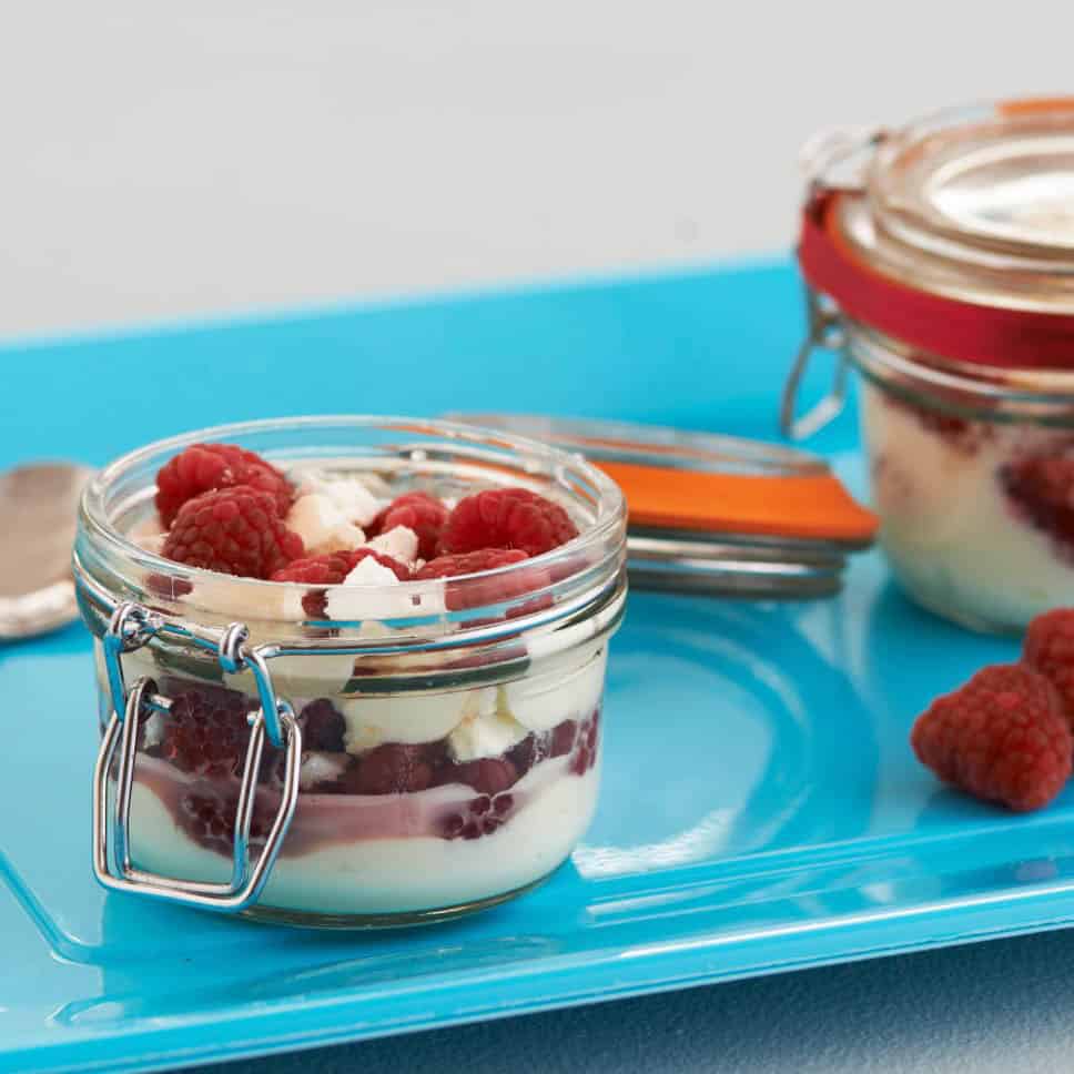 Kilner glasburk fylld med en dessert av färska hallon, grädde och maräng, serverad på ett blått fat.
