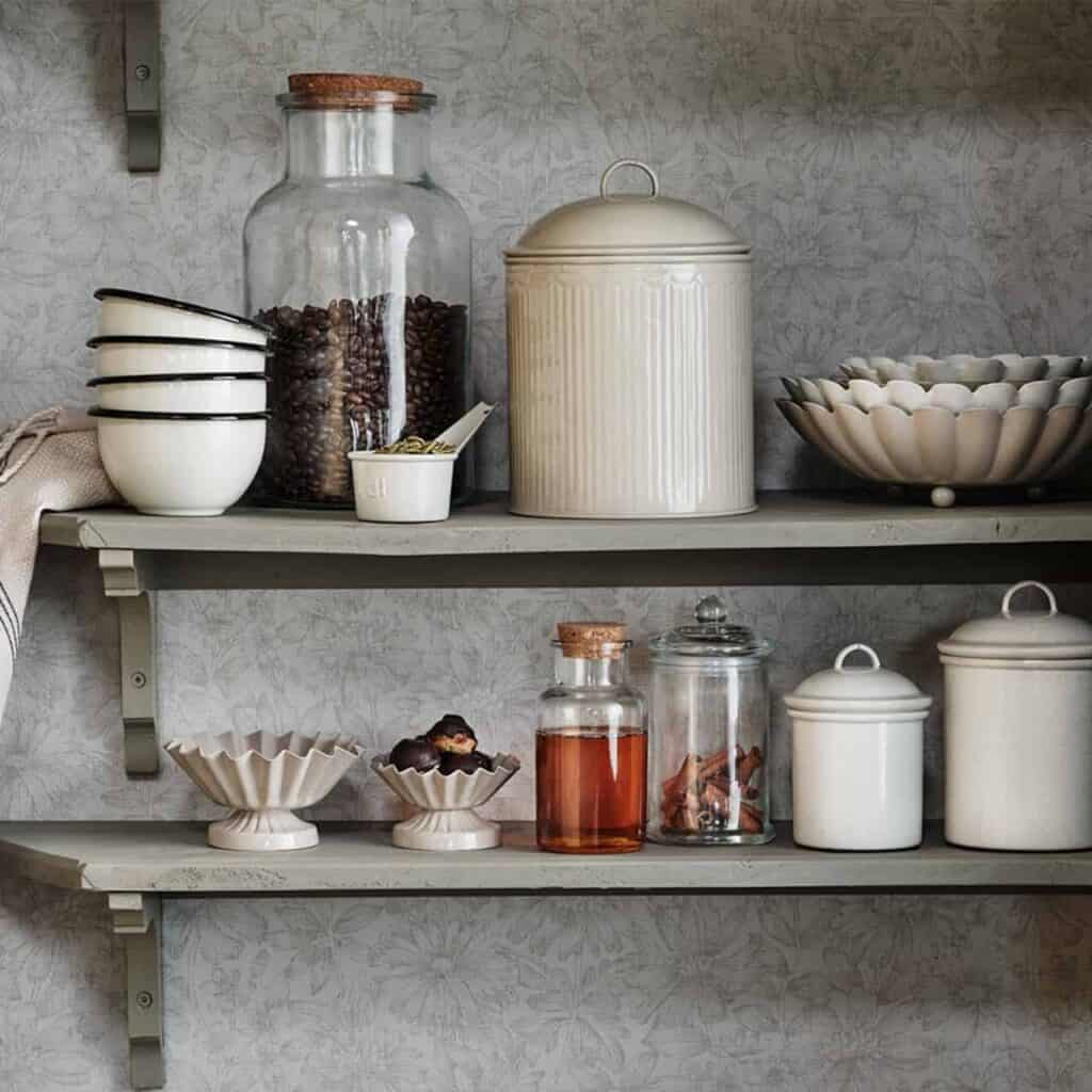 Stilfull kökshylla med öppna hyllplan, fylld med glasburkar, plåtburkar och porslin i harmoniska beige toner, skapar en charmig och organiserad känsla.