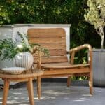 Loungefåtölj i teak placerad på en solig uteplats, omgiven av grönska och dekorerad med ett litet sidobord och blomvas.
