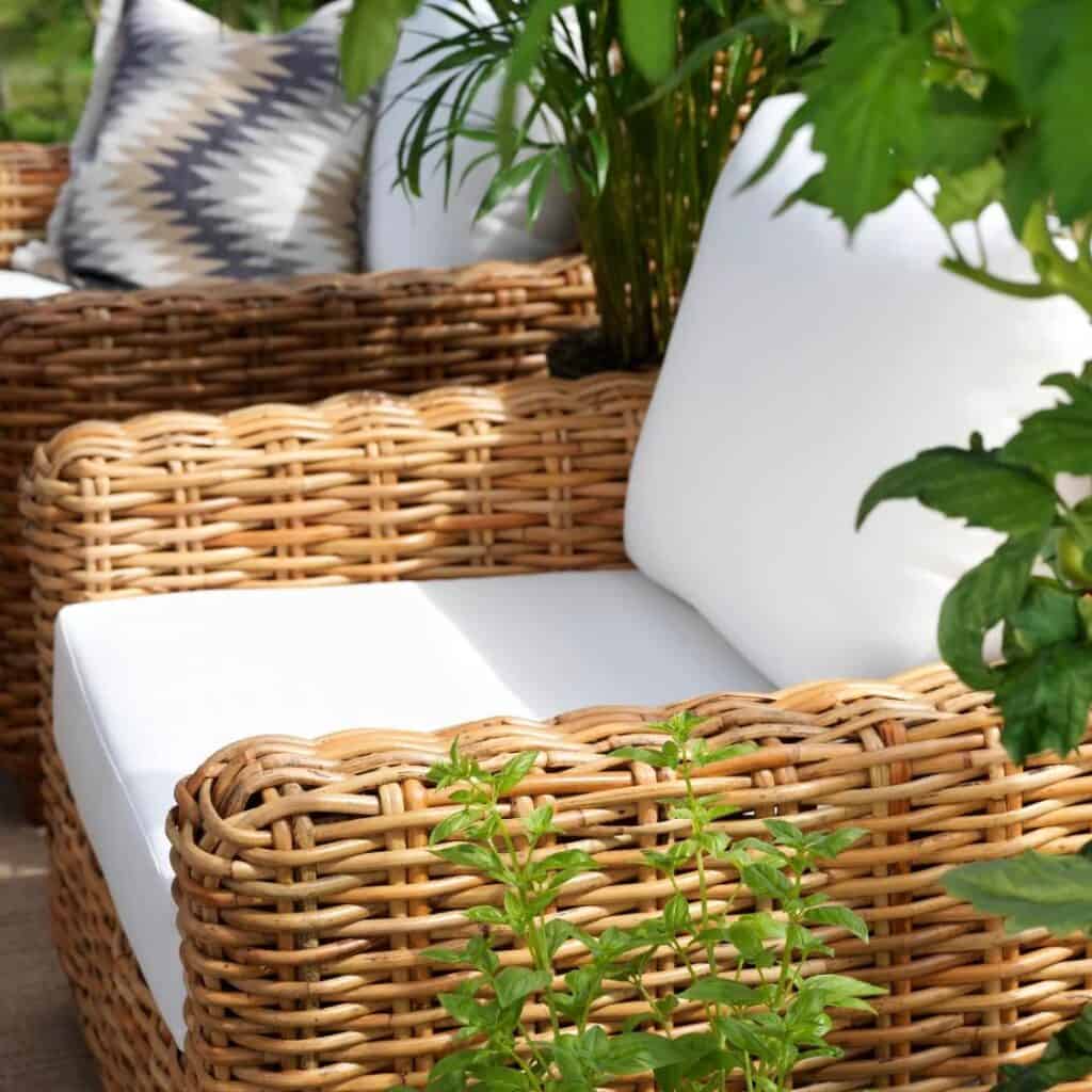 Rossvik loungeset i handflätad naturrotting med vita dynor, bestående av en soffa, två fåtöljer och ett stilrent soffbord med glas- och trädetaljer.