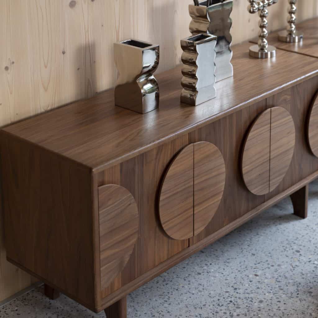Sidobord Groove i valnötsfanér med tre dörrar och runda designmönster, dekorerat med moderna silvervaser och ljusstakar.