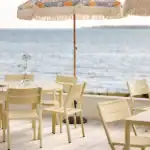 Flera DELIA matstolar i lemon uppställda runt runda bord på altan med havsutsikt.