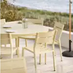 Närbild på DELIA matstolar i lemon runt ett runt bord på altan nära stranden.