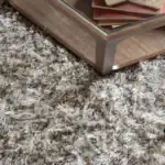 Närbild på matta Hairy från Zuiver, visad tillsammans med ett soffbord i trä för att lyfta fram mattans fluffiga garn och naturliga ton.