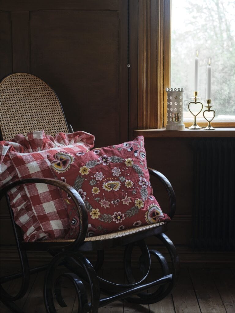 Adventsstämning hemma med enkel dekoration – kudde i röda toner och tända ljus i fönstret.