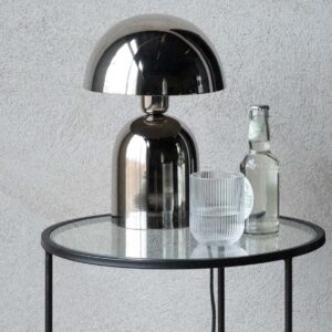 Bordslampa i krom – ROME från Wikholm Form på glasbord, i modern miljö med dryck och glas bredvid.