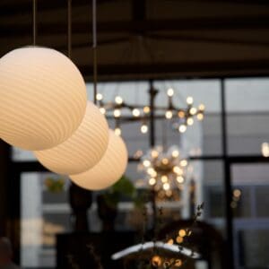 Taklampa SETH Nordal i mattvitt glas med randigt mönster och mässingsdetaljer, tre lampor i rad som sprider varmt ljus i en inredd miljö.