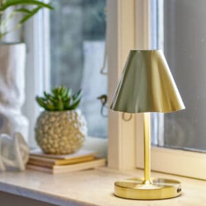 Laddningsbar lampa i mässing från Bloomingville, Lianna – står på ett fönsterbräde och sprider varmt ljus.