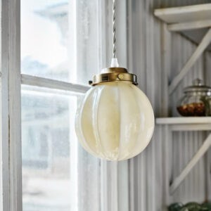 Taklampa Marit i mässing och beige opalglas hängande i fönster – sprider varmt ljus med klassisk charm.