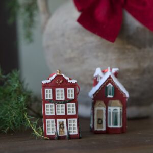 Rött miniatyrstadshus som juldekoration från Hemlängtan, fotograferat i en varm miljö med granris och juldetaljer.