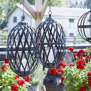 TORUN hänglykta i antiksvart järn hänger på en altan med röda pelargoner.