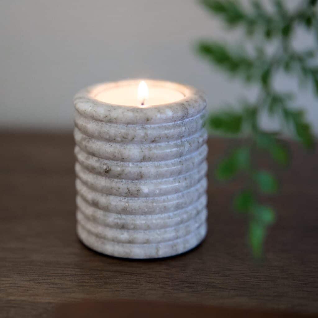 Värmeljuslykta OTOK i beige marmor med tänt ljus – varm och naturlig känsla.