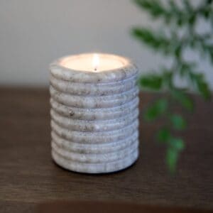 Värmeljuslykta OTOK i beige marmor med tänt ljus – varm och naturlig känsla.