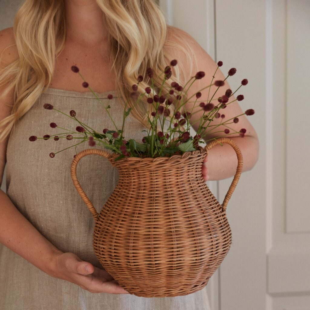 Person håller vas i rotting fylld med blommor