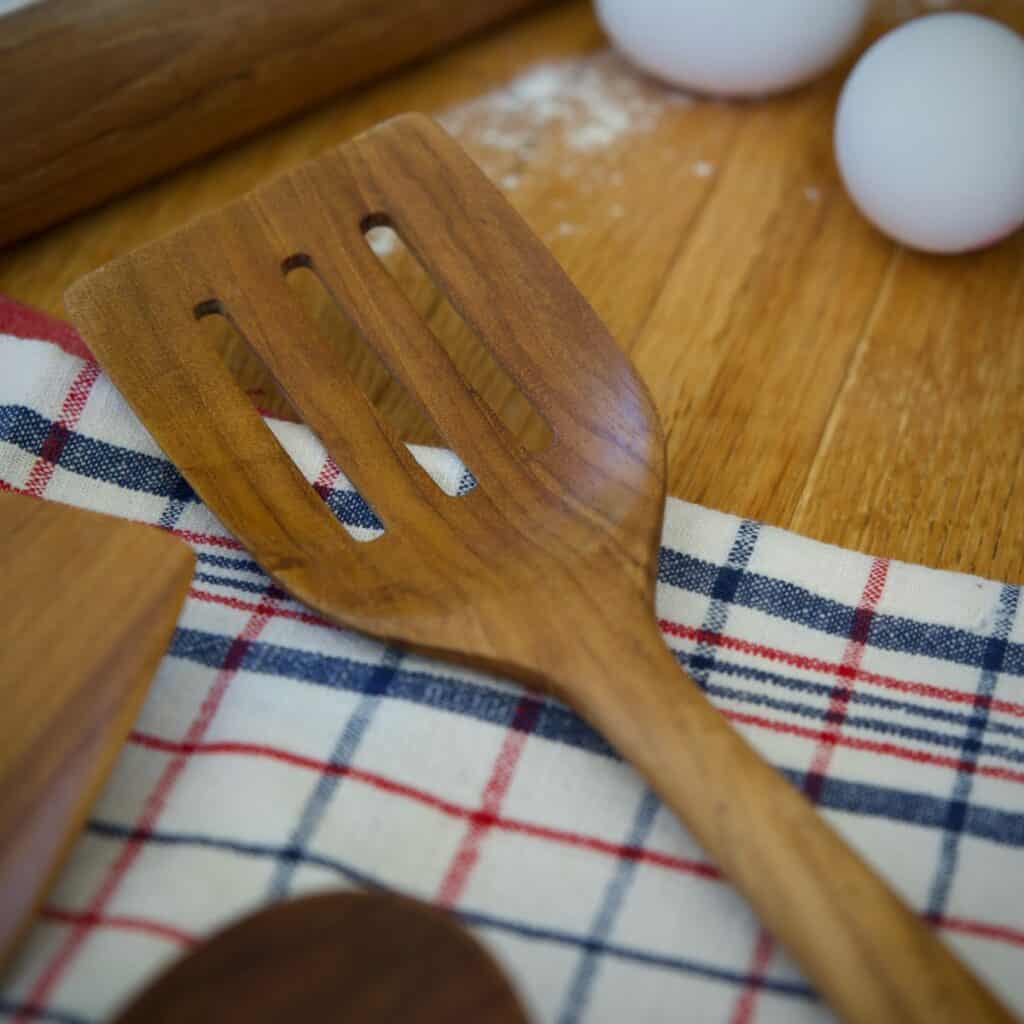 Perforerad stekspade i teak från Nordhamn på rutig kökshandduk med ägg och mjöl på träbänk.