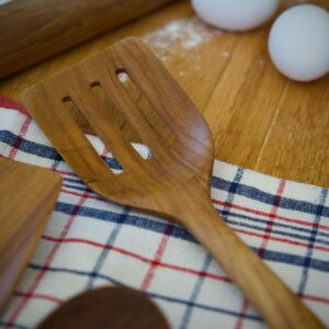 Perforerad stekspade i teak från Nordhamn på rutig kökshandduk med ägg och mjöl på träbänk.