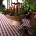 Randig duk Svea i rött och naturvitt med julkaka på träfat, dekorerad med glasyr, röda bär och gröna kvistar.